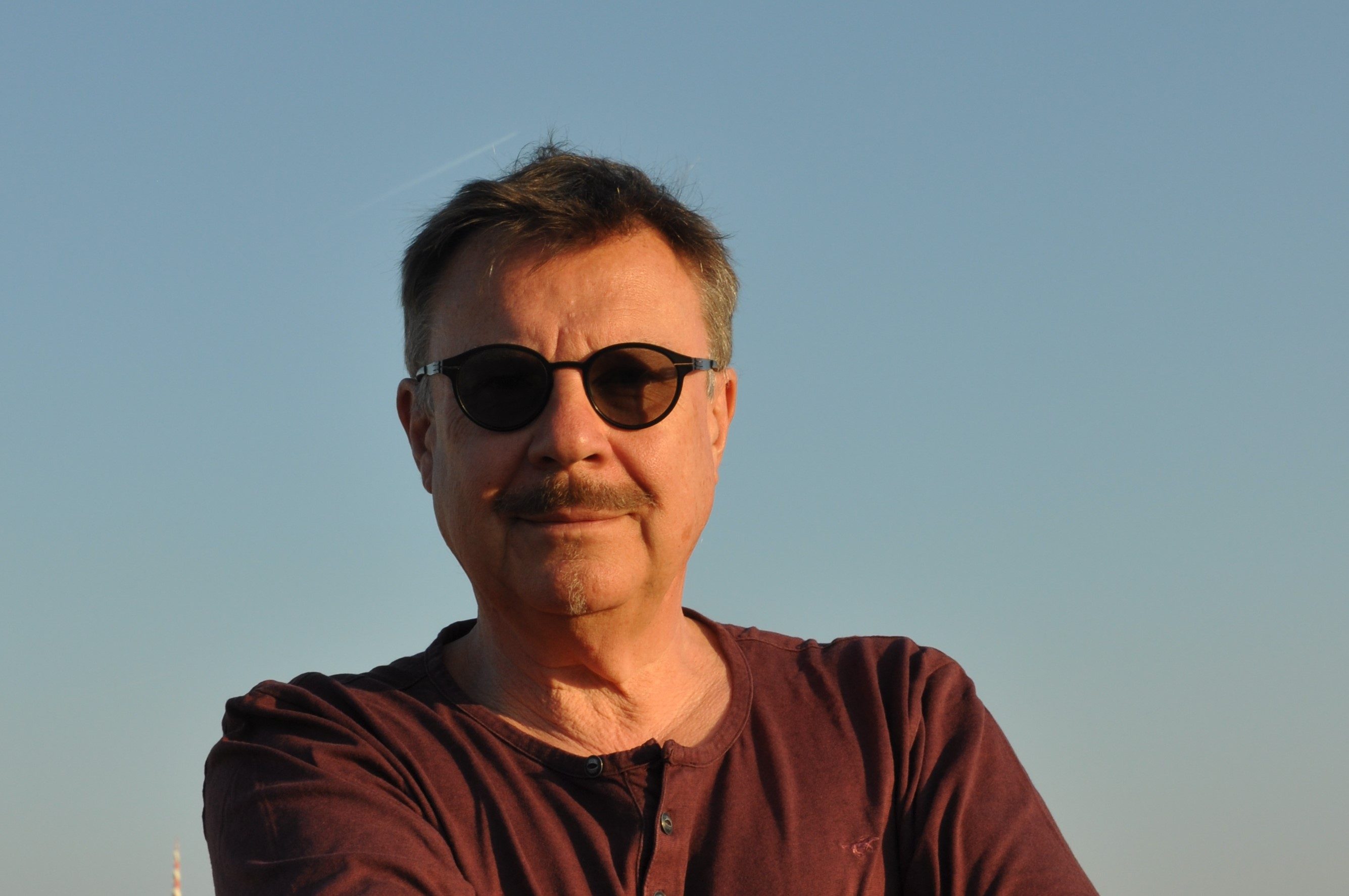 Johannes C. Hoflehner, Porträt mit Sonnenbrille vor blauem Himmel